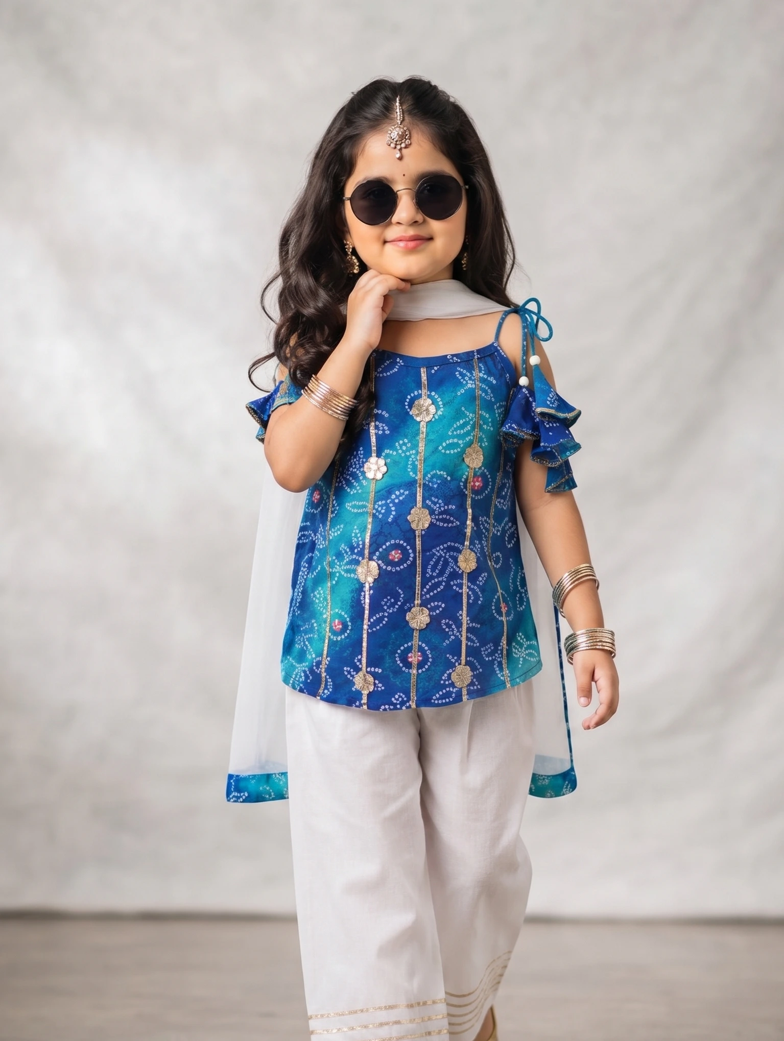 Girls Blue Festive 3-Piece Kurti with White Pants & Dupatta Set Little girl wearing a blue printed pure cotton festive kurti adorned with intricate Gota patti work, paired with white pants featuring a Gota border and a sheer matching dupatta.